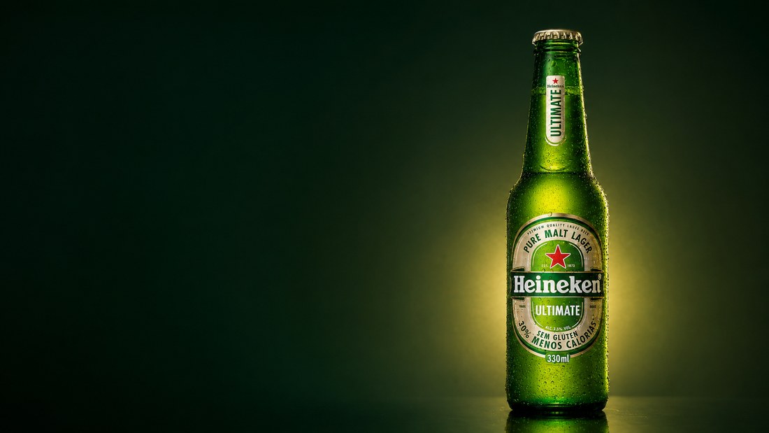 Garrafa long neck Heineken Ultimate gelada em fundo verde escuro, com luz de estúdio.